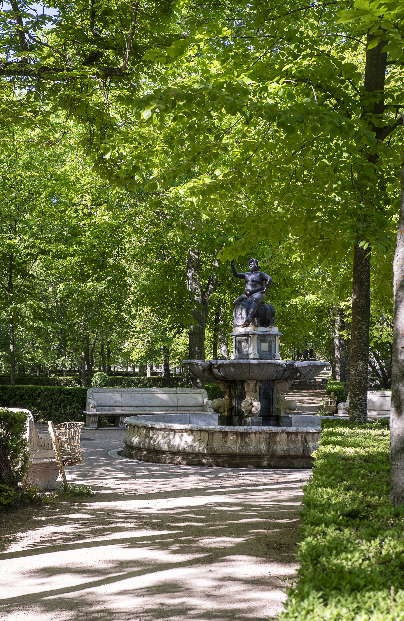 Fotografía de una fuente con figura de bronce en un paseo arbolado del jardín.