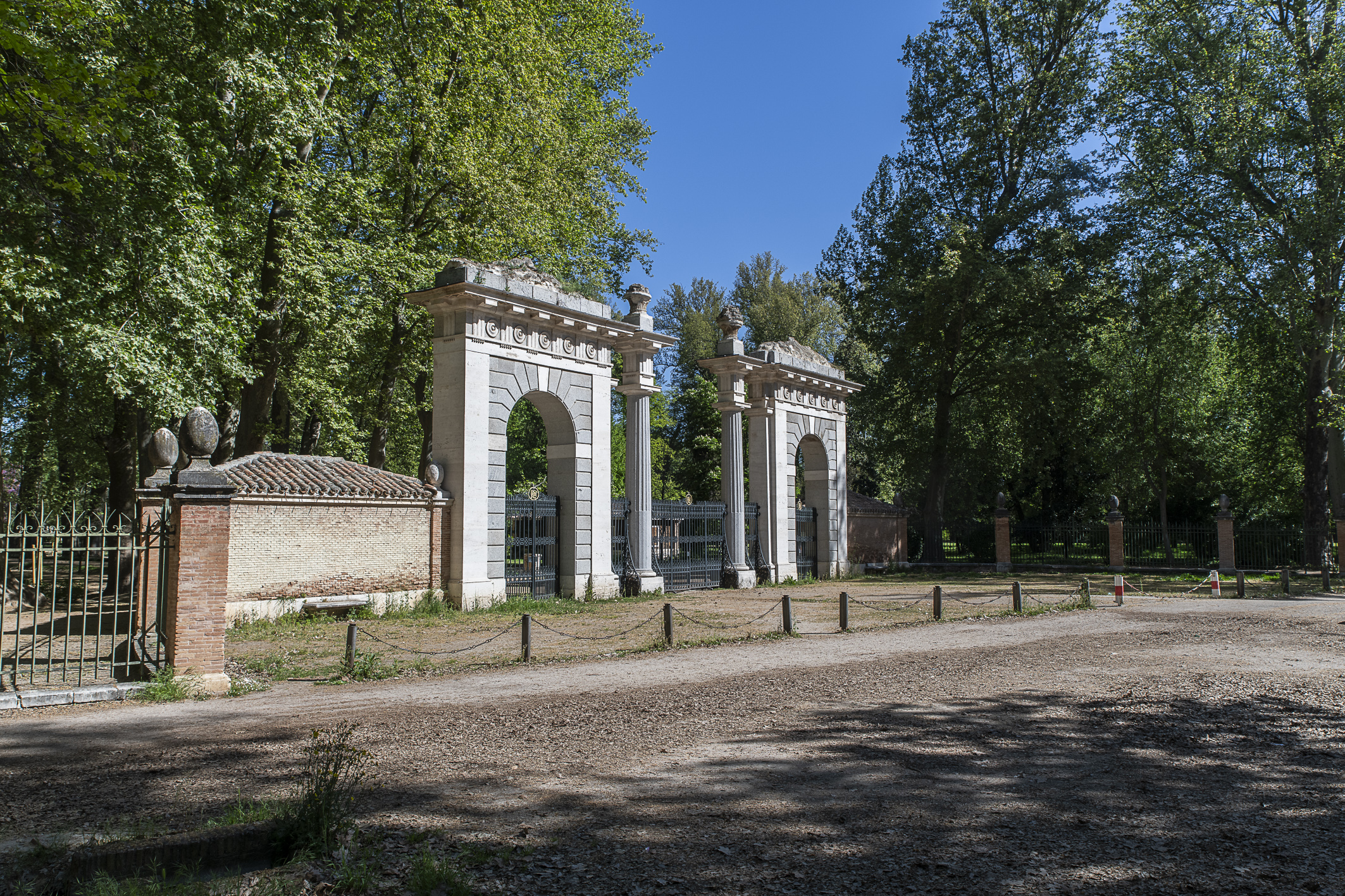 Fotografía de una puerta monumental de tres arcos en el jardín, entre arboleda.