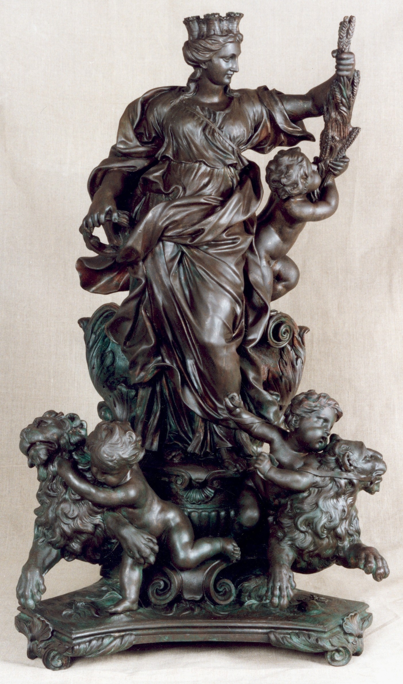Escultura de bronce de una figura femenina coronada con niños y leones.