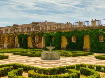 Fotografía de un jardín con fuente central, setos de boj recortados y galería porticada.