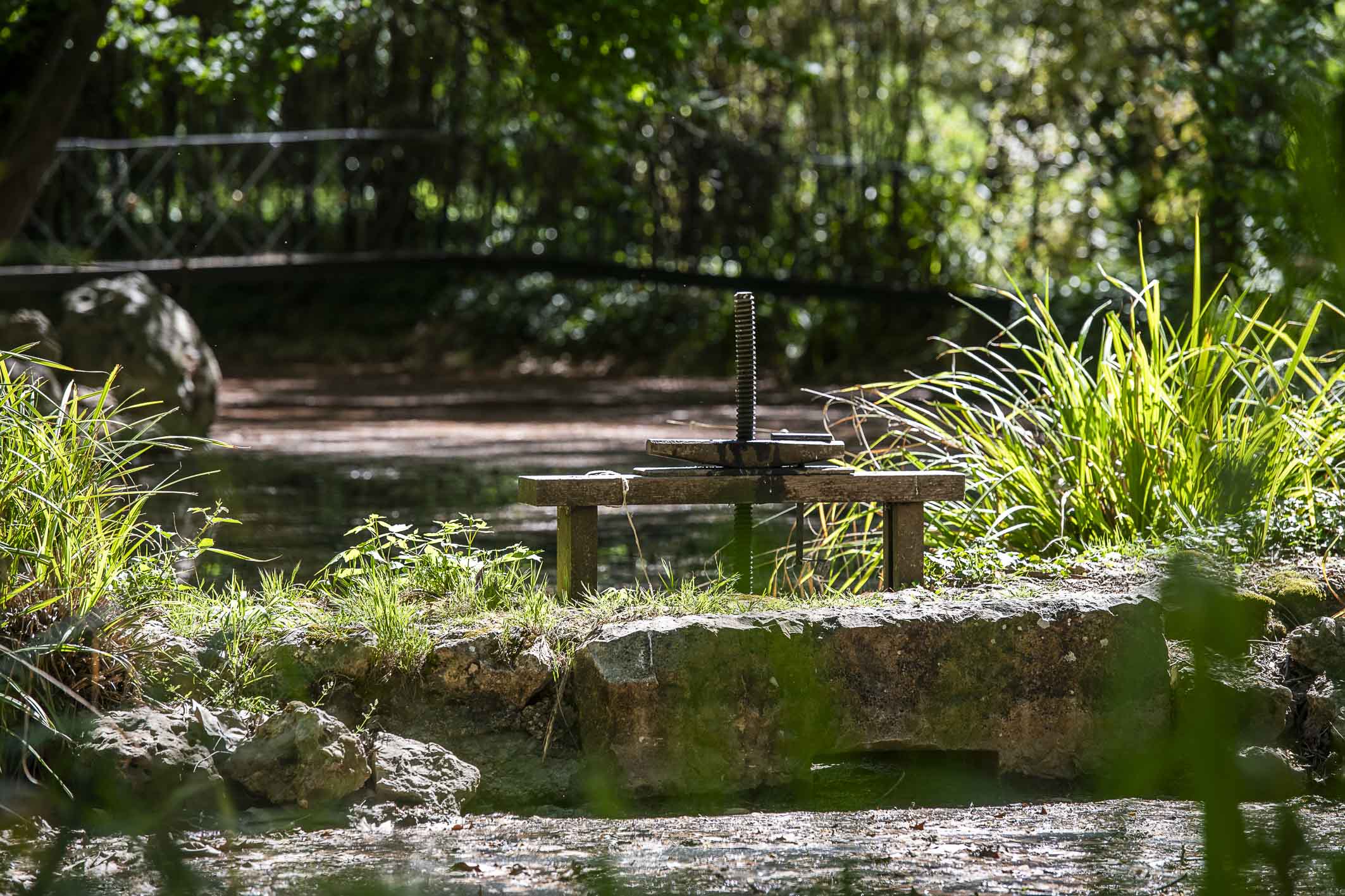 Fotografía de una antigua compuerta con husillo de hierro junto a un canal del jardín.