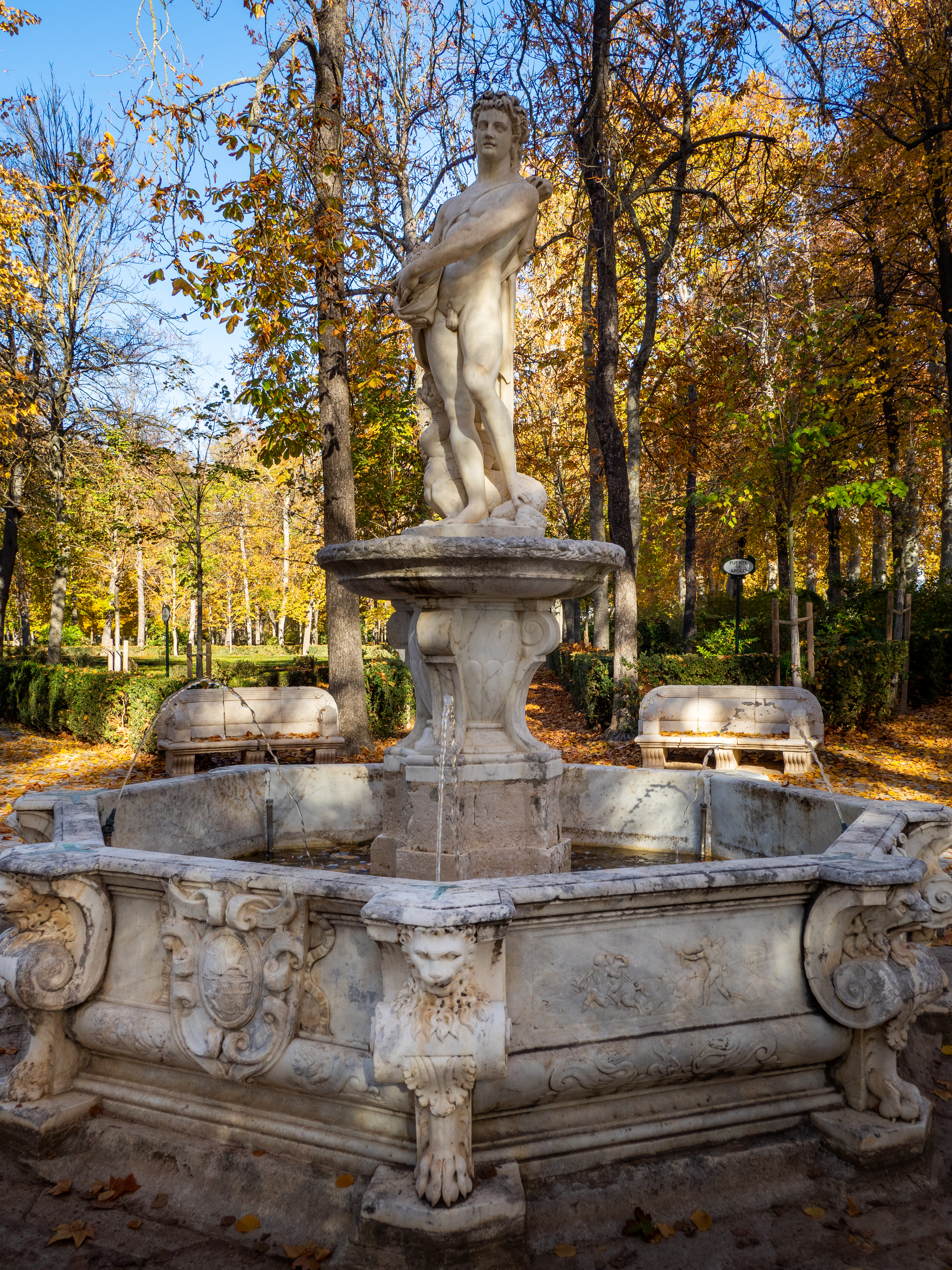 Fotografía de una fuente de mármol con una estatua masculina, en un jardín otoñal.